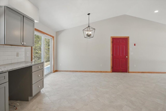 kitchen featuring baseboards, an inviting chandelier, gray cabinets, backsplash, and lofted ceiling