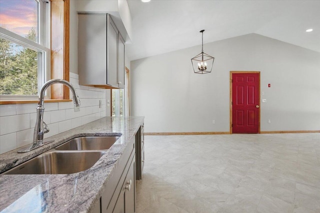 kitchen with baseboards, vaulted ceiling, gray cabinets, backsplash, and a sink