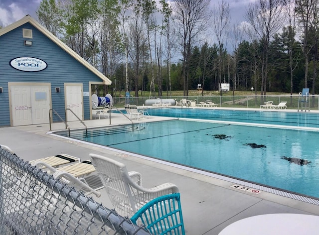 community pool with fence, a patio, and view of scattered trees