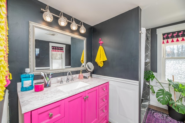 bathroom featuring a decorative wall, visible vents, wainscoting, and vanity