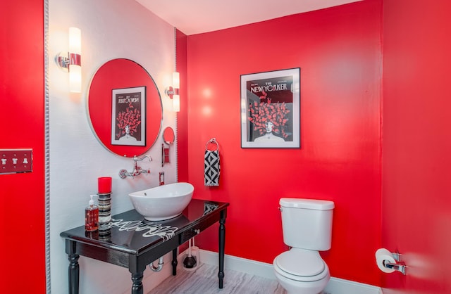 half bathroom featuring wood finished floors, toilet, baseboards, and a sink