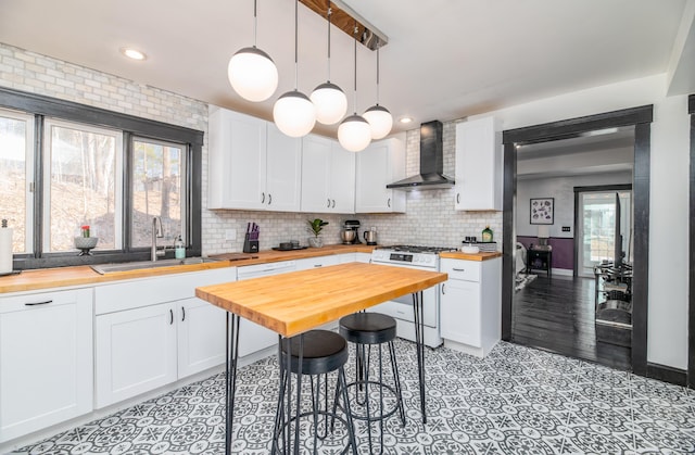 kitchen featuring butcher block counters, wall chimney range hood, white cabinets, white range with gas cooktop, and a sink