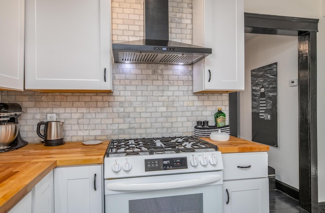 kitchen with wood counters, wall chimney range hood, white cabinetry, decorative backsplash, and white range with gas cooktop