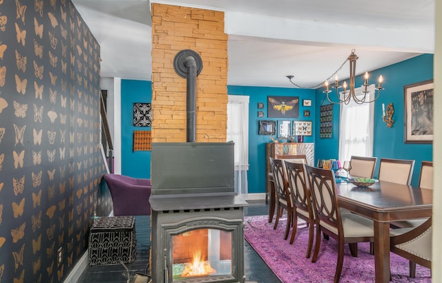 dining space featuring wood finished floors, a chandelier, a wood stove, and baseboards