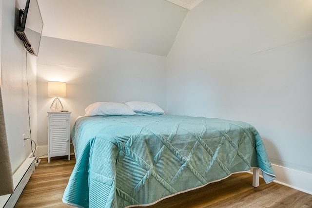 bedroom with a baseboard radiator, vaulted ceiling, and wood finished floors