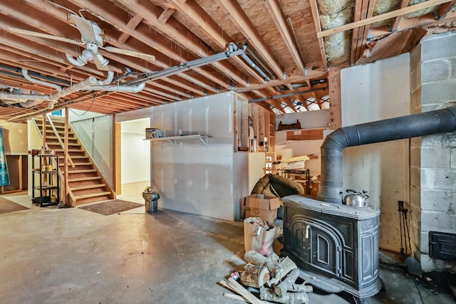 below grade area featuring concrete block wall, a wood stove, and stairway