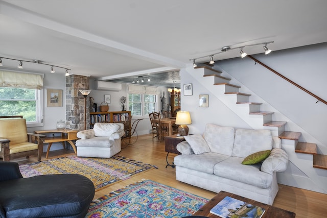living room featuring stairs, wood finished floors, a wall unit AC, rail lighting, and a wealth of natural light