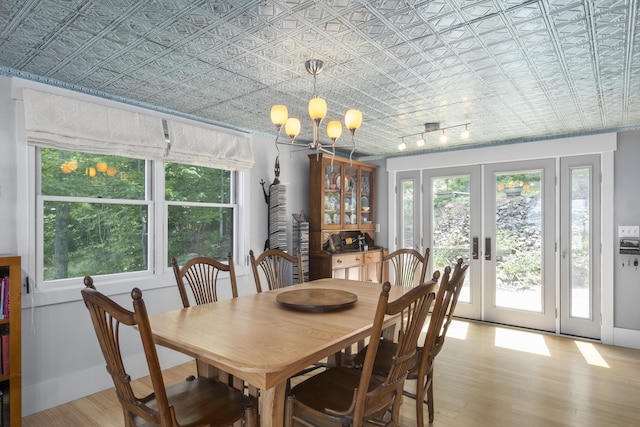 dining space with an ornate ceiling, a chandelier, french doors, and light wood finished floors