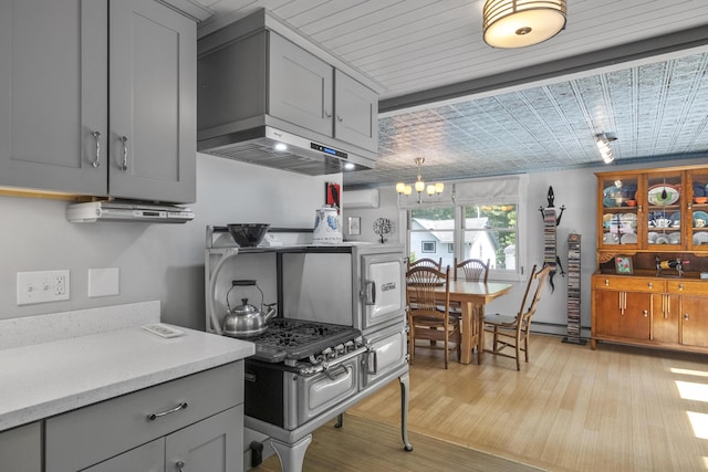 kitchen with range hood, light countertops, gray cabinets, light wood finished floors, and a notable chandelier