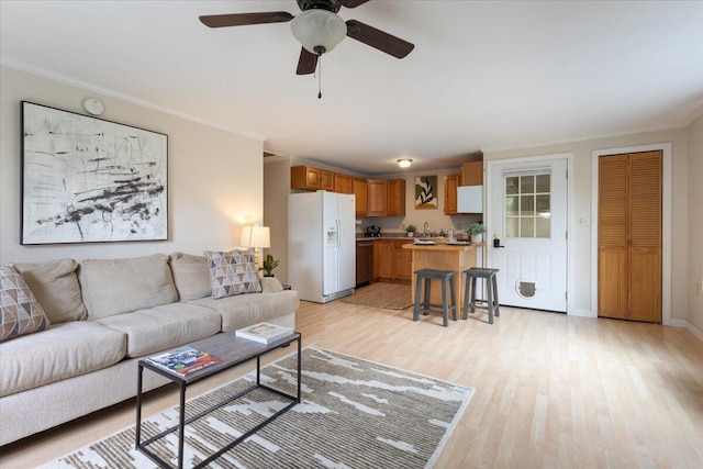 living room with ornamental molding, light wood-type flooring, a ceiling fan, and baseboards