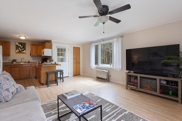 living area with light wood-style flooring, a ceiling fan, baseboards, and heating unit