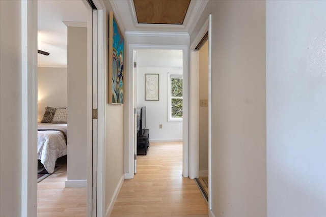 corridor with light wood-style floors, ornamental molding, and baseboards