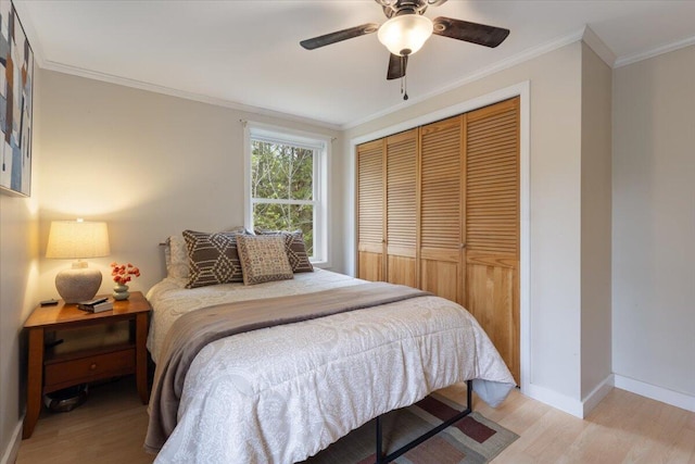 bedroom with a closet, light wood-type flooring, ornamental molding, baseboards, and a ceiling fan