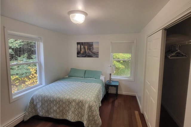 bedroom with baseboard heating, multiple windows, dark wood-style flooring, and a closet