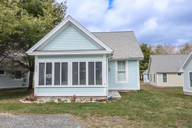 rear view of house featuring a shingled roof and a yard