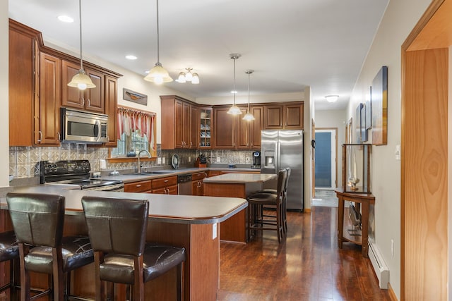 kitchen with a sink, appliances with stainless steel finishes, a peninsula, a kitchen bar, and a baseboard heating unit