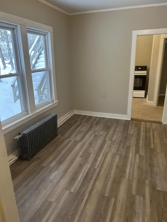 spare room featuring baseboards, wood finished floors, crown molding, and radiator