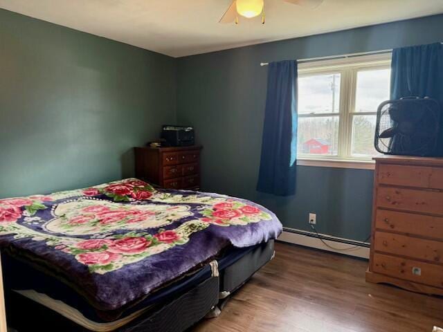 bedroom featuring a ceiling fan, wood finished floors, and baseboard heating