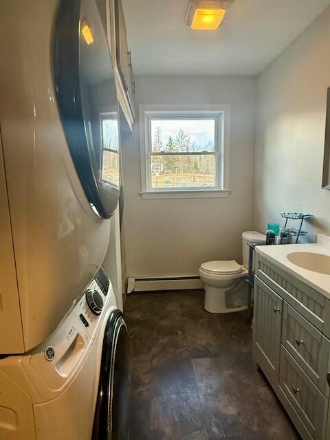 bathroom featuring toilet, vanity, stacked washing maching and dryer, and baseboard heating
