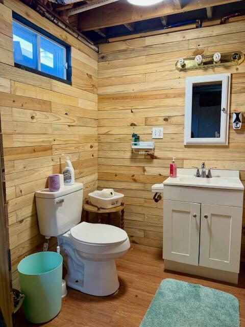 bathroom featuring toilet, vanity, wood walls, and wood finished floors