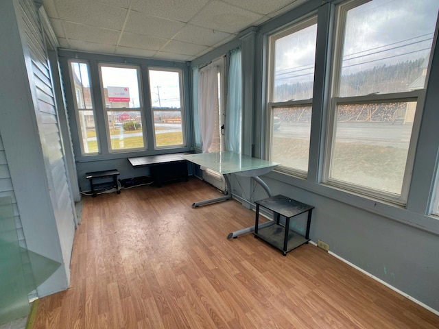 unfurnished sunroom with baseboards, wood finished floors, and a paneled ceiling