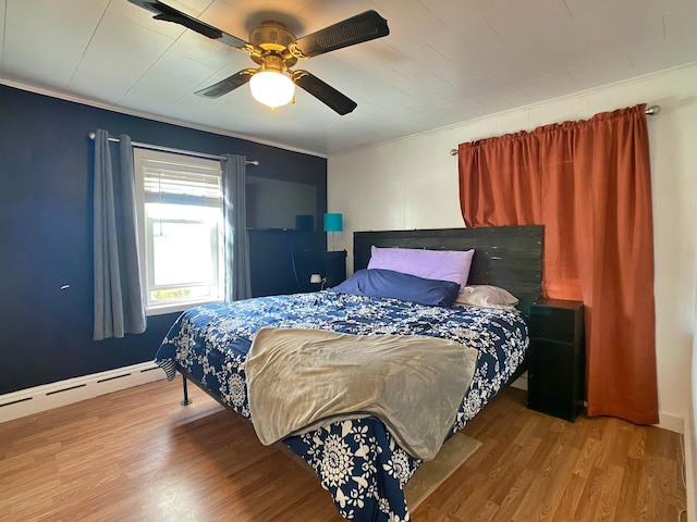 bedroom featuring a ceiling fan, wood finished floors, a baseboard heating unit, and crown molding
