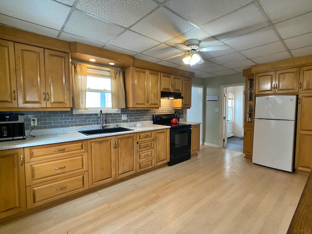 kitchen with black electric range oven, a sink, light countertops, and freestanding refrigerator