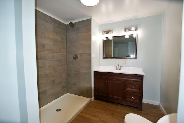 full bathroom with toilet, wood finished floors, vanity, baseboards, and tiled shower