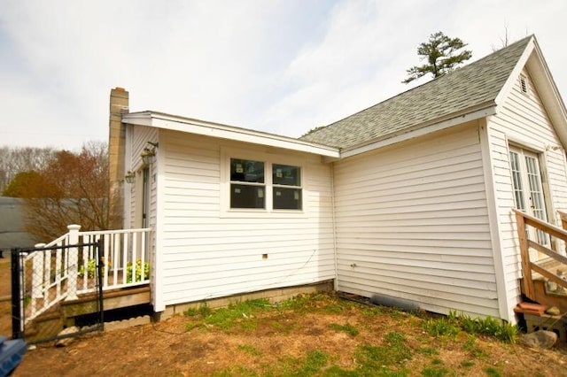 view of property exterior with a shingled roof and a chimney