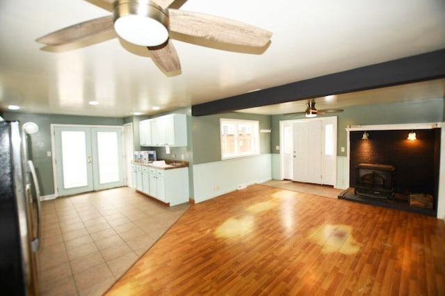 unfurnished living room with wood finished floors, beam ceiling, ceiling fan, and french doors