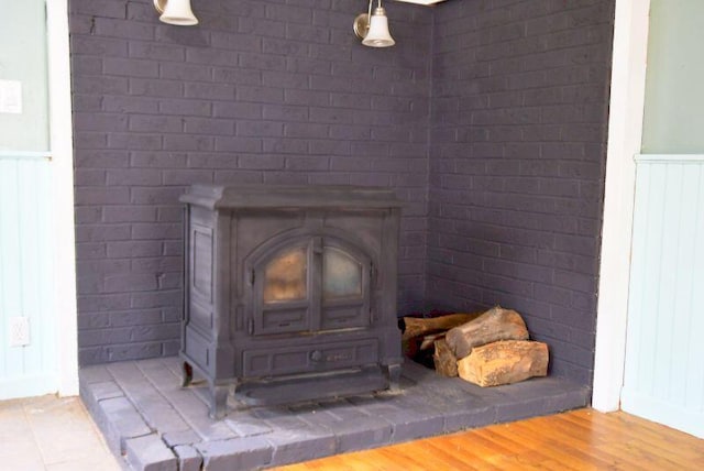 details featuring a wood stove, wood finished floors, and a wainscoted wall