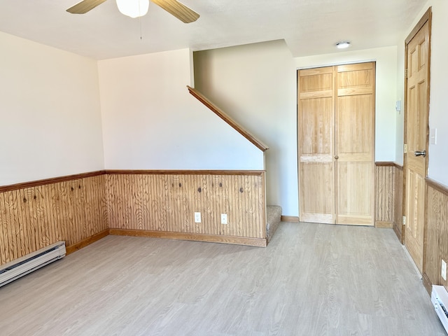 unfurnished room featuring wainscoting, wooden walls, ceiling fan, a baseboard radiator, and wood finished floors