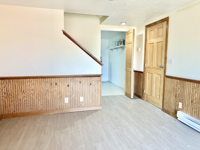 spare room with a wainscoted wall, a baseboard radiator, wooden walls, and light wood-style flooring