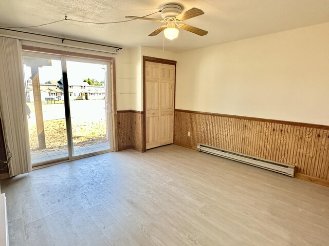 spare room featuring a wainscoted wall, wooden walls, baseboard heating, light wood-style floors, and ceiling fan