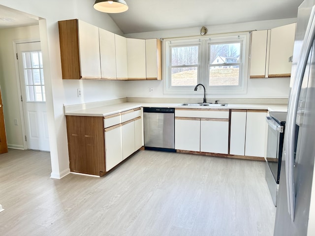 kitchen with light countertops, light wood-style flooring, appliances with stainless steel finishes, a sink, and vaulted ceiling