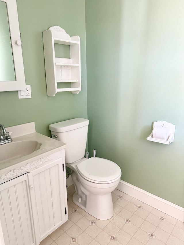half bathroom with toilet, vanity, tile patterned flooring, and baseboards