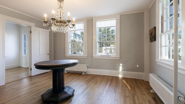 unfurnished dining area featuring hardwood / wood-style floors, radiator, an inviting chandelier, and baseboards