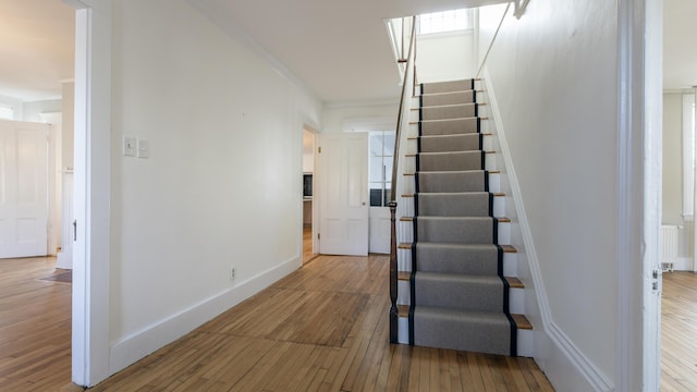 stairway with hardwood / wood-style floors, ornamental molding, baseboards, and radiator heating unit