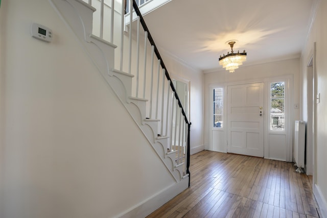 entrance foyer with radiator, stairs, an inviting chandelier, ornamental molding, and hardwood / wood-style flooring