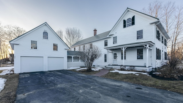 view of front of house with driveway, a chimney, a garage, and a porch