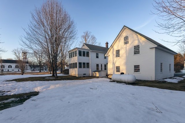 snow covered rear of property with a sunroom