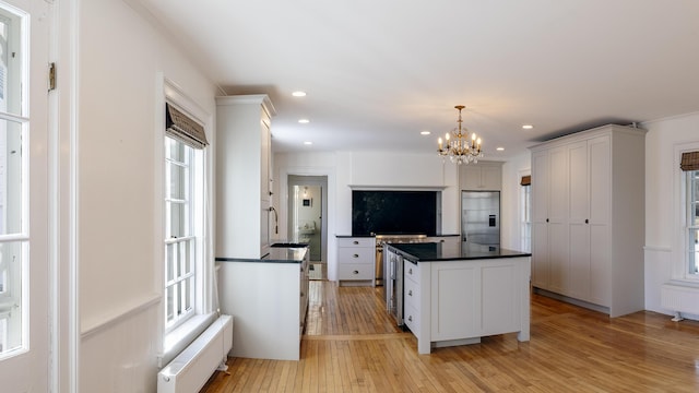 kitchen featuring stainless steel built in refrigerator, a chandelier, dark countertops, light wood finished floors, and radiator heating unit