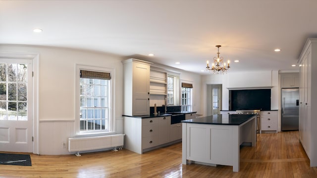 kitchen with a chandelier, radiator heating unit, stainless steel built in fridge, light wood-style flooring, and dark countertops