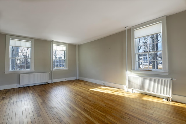 spare room featuring hardwood / wood-style floors, baseboards, radiator heating unit, and radiator