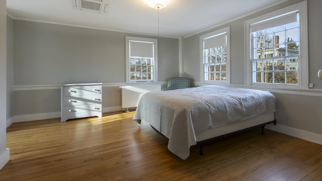 bedroom with ornamental molding, light wood finished floors, and radiator