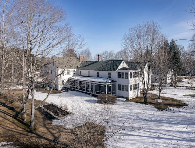 snow covered back of property with a sunroom, a chimney, and metal roof
