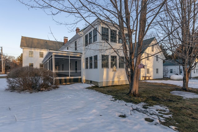 snow covered house with a sunroom and a chimney