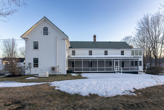 snow covered house featuring metal roof, a sunroom, a chimney, and ac unit