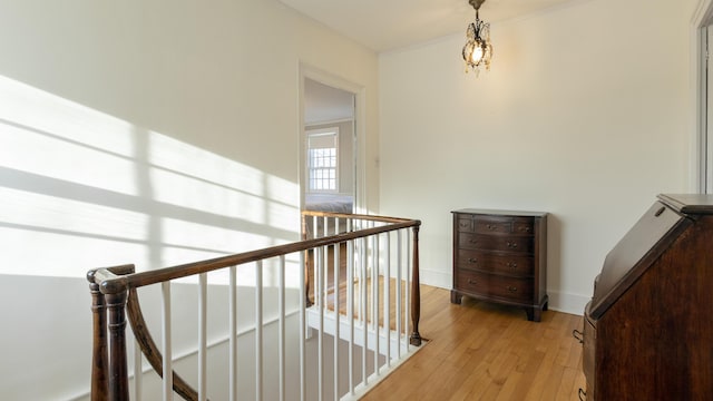 corridor featuring baseboards, an upstairs landing, light wood-style flooring, and ornamental molding