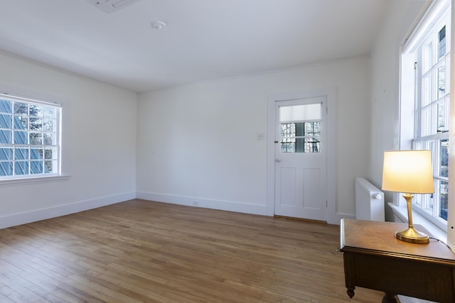 interior space with baseboards, ornamental molding, radiator heating unit, and light wood-type flooring